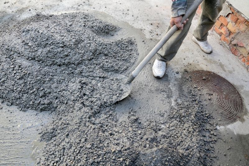 a picture of a person holding a shovel mixing the concrete on the ground