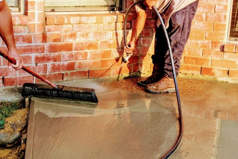 person holding a water hose pouring water to a concrete ground