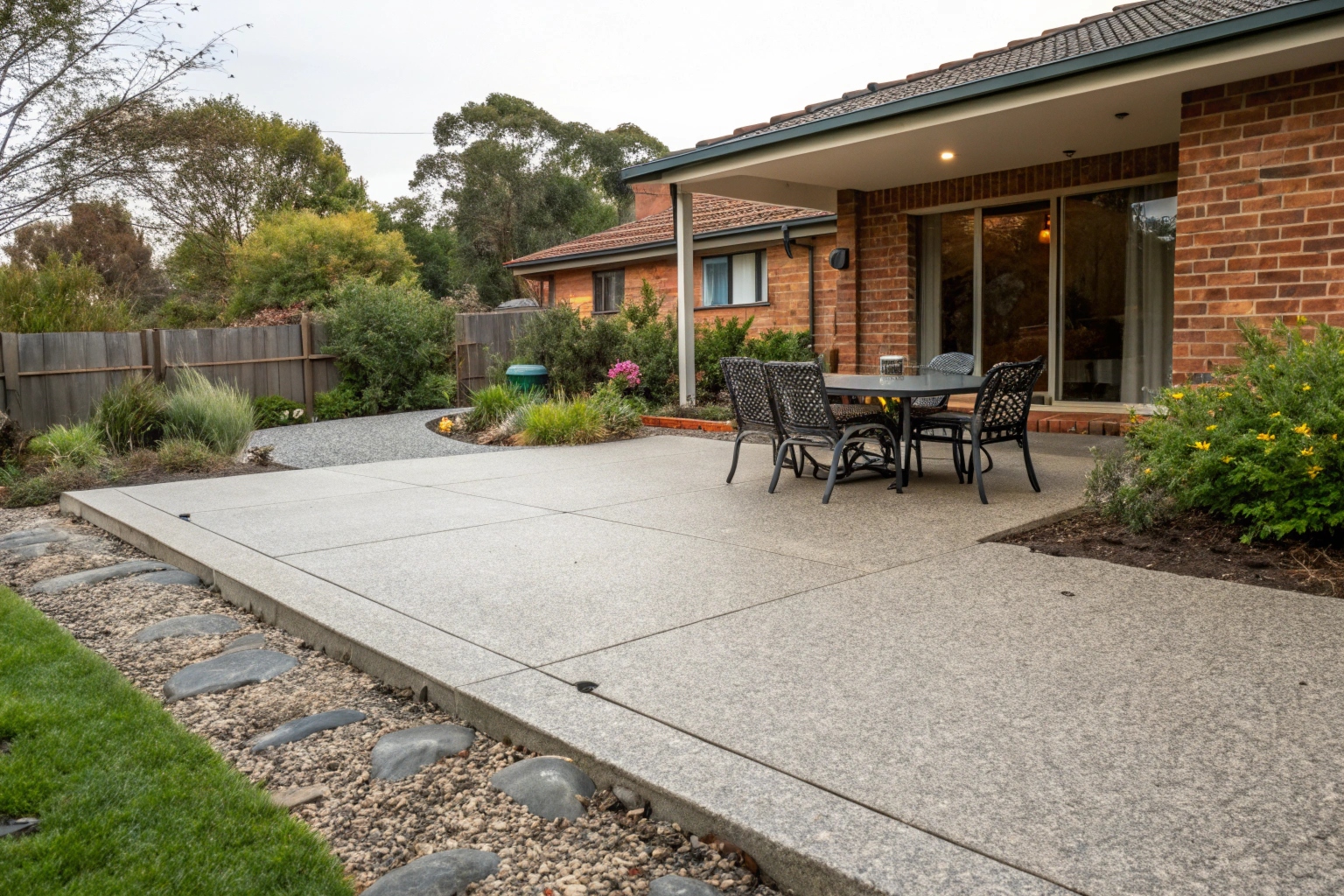 Exposed aggregate concrete patio slab with outdoor dining setup behind Newcastle home